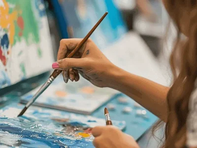 Close-up-of-a-young-artists-hands-painting-vivid-details-on-a-canvas-with-brushes-and-abstract-artwork-in-the-background